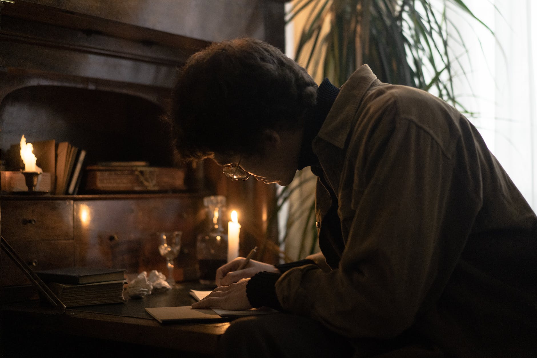 focused man writing on paper beside a candlelight
